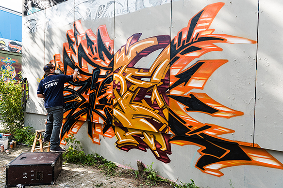 A grafitti artist paints a bold, graphic orange and black piece of artwork on a wall