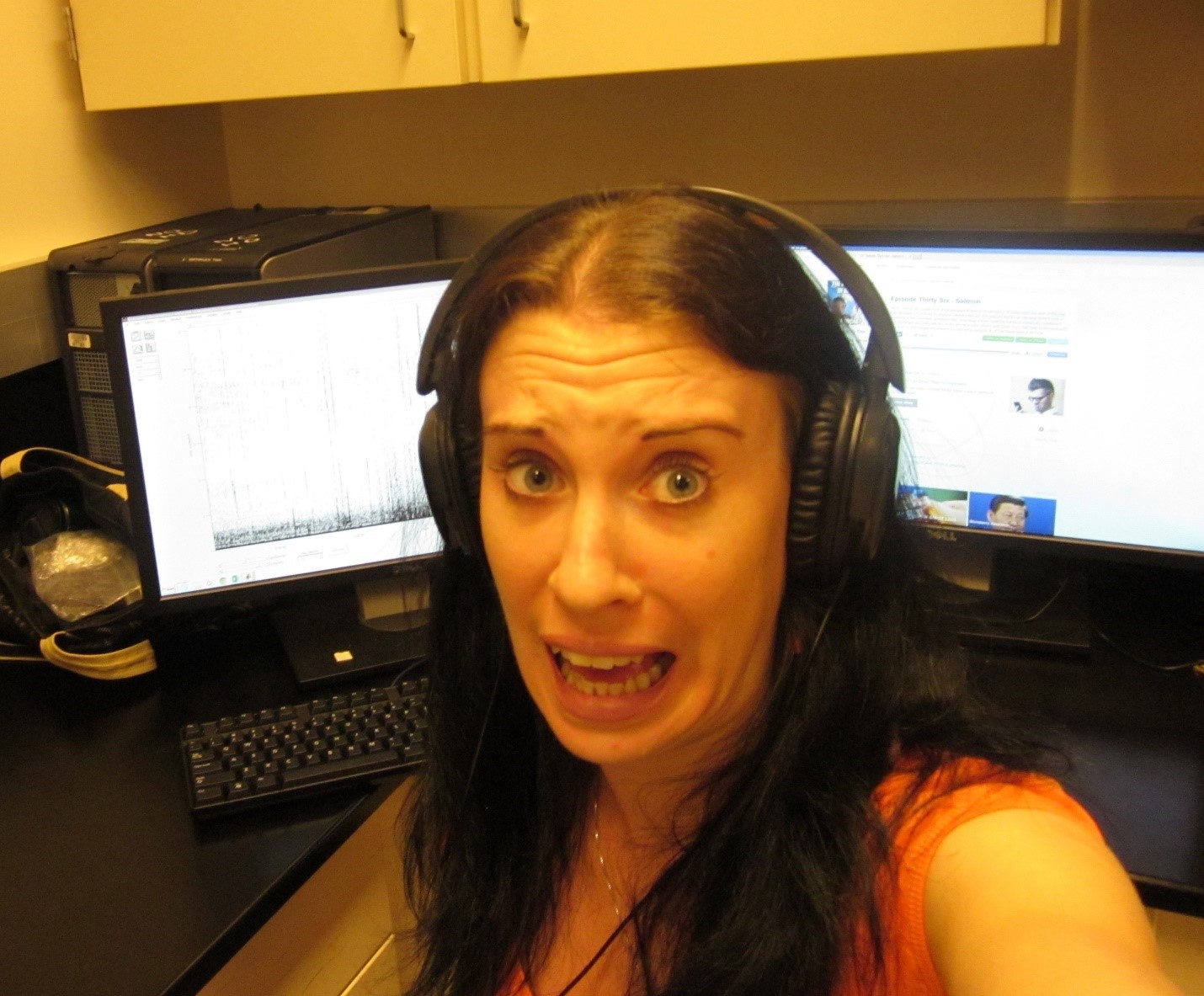 A girl wearing headphones and sitting in front of two monitors with a distressed expression on her face.