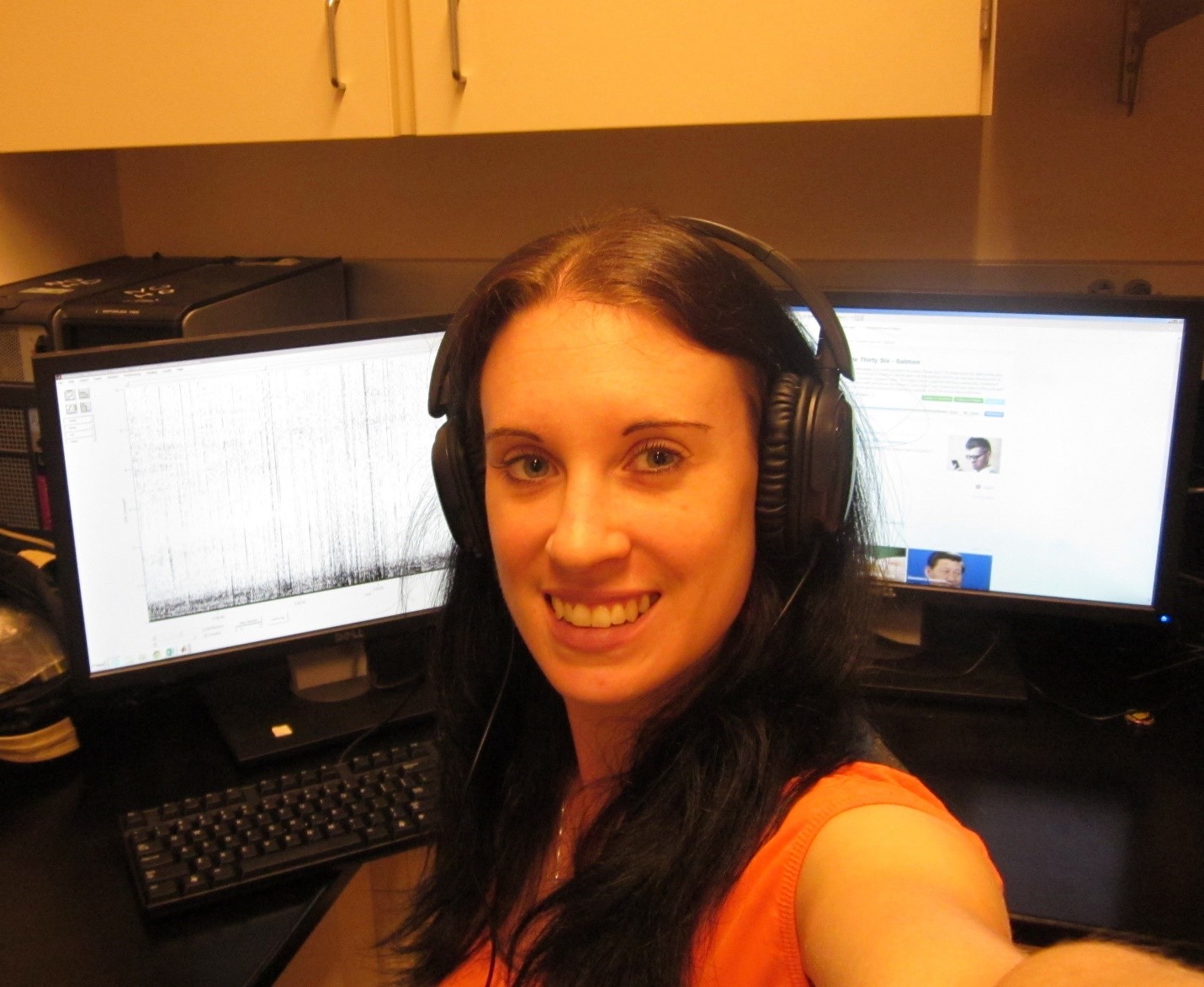 A girl wearing headphones and sitting in front of two monitors with a satisfied smile on her face.