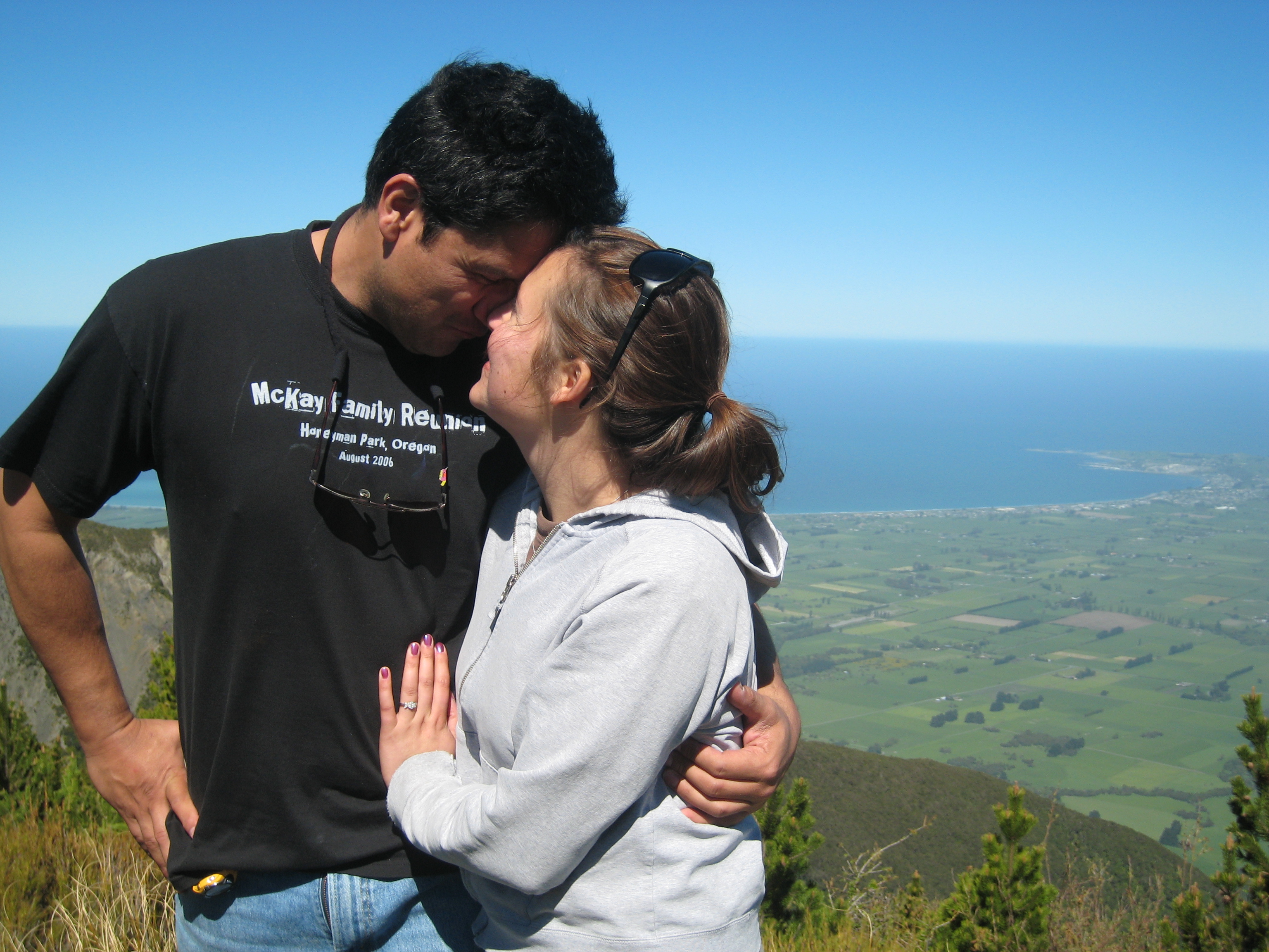 A man in a black shirt and a woman in a grey sweatshirt standing together on a grassy hill.