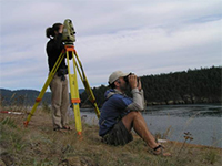 Two marine biologists using survey equipment along the side of a body of water.