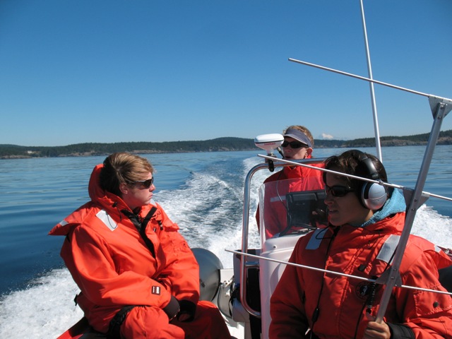 Three people in bright orange coats on a boat