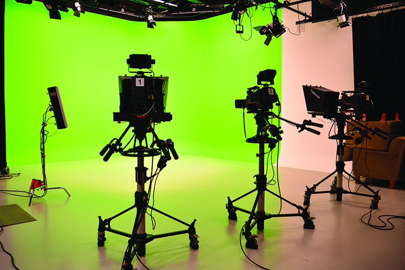 a set of high end video cameras and lights point towards a green screen