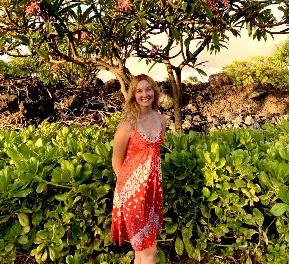 Madison Guard poses in front of a tropical tree; a sandy beach is behind her 