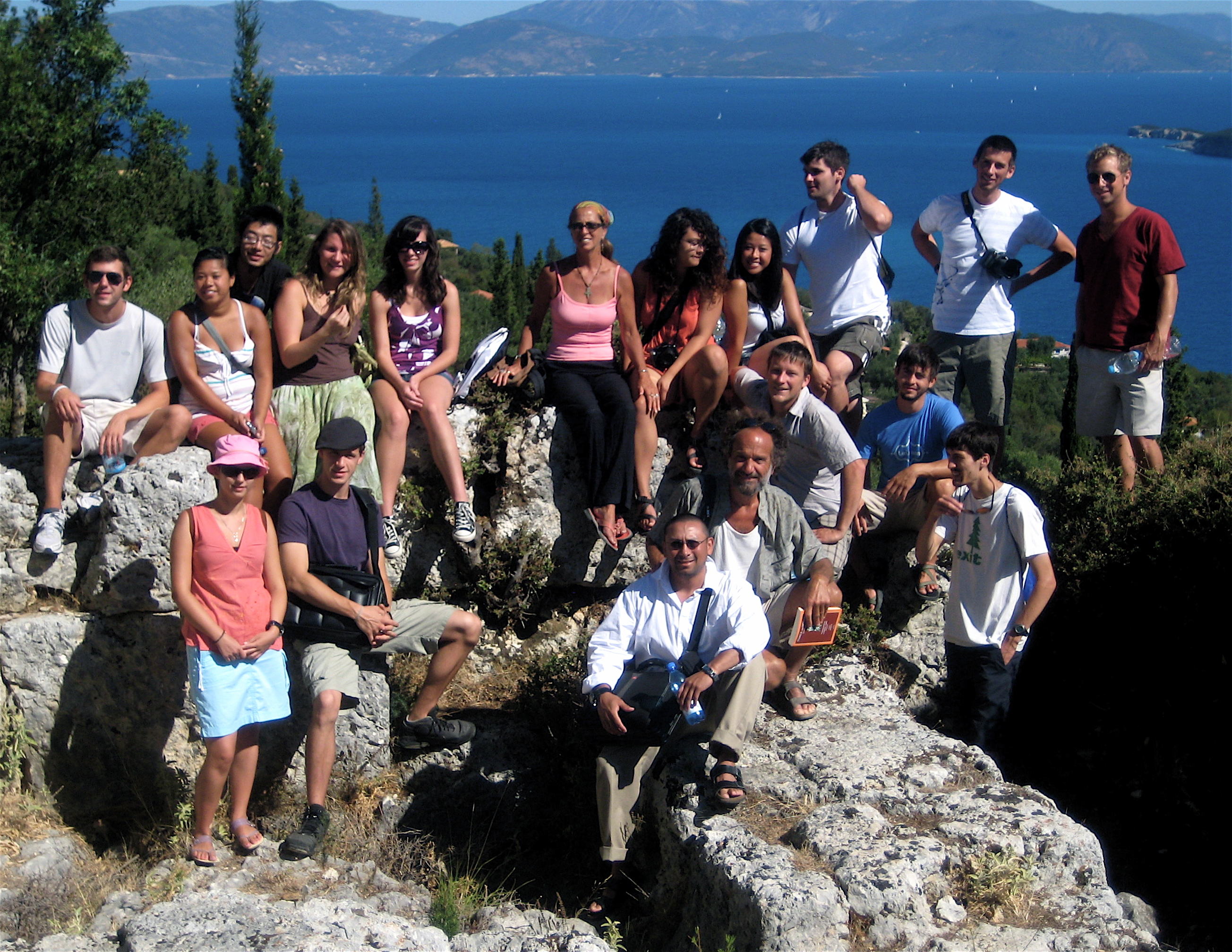 A group of students sitting on large rocks by the coast, with several islands in the distance.