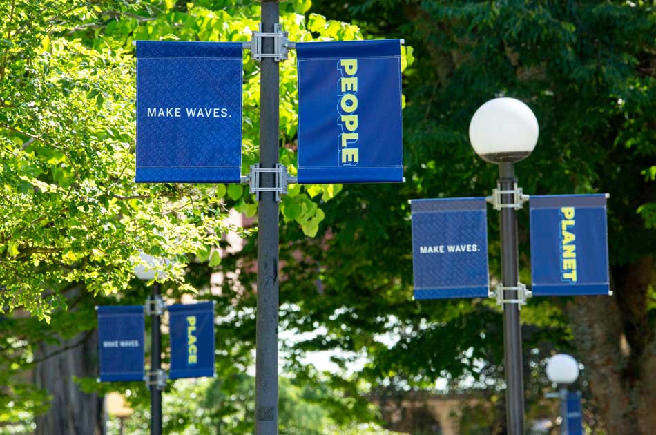 Three light post banners line the walkway leading to Old Main  reading People, Planet, Place.