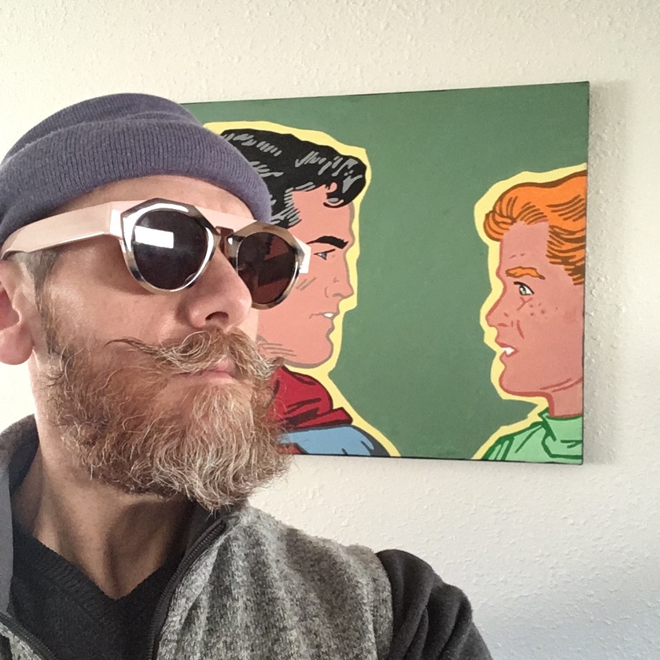 Chris wears a purple beanie and retro sunglasses with chunky frames. He stands in front of a Superman painting, facing the same direction. 