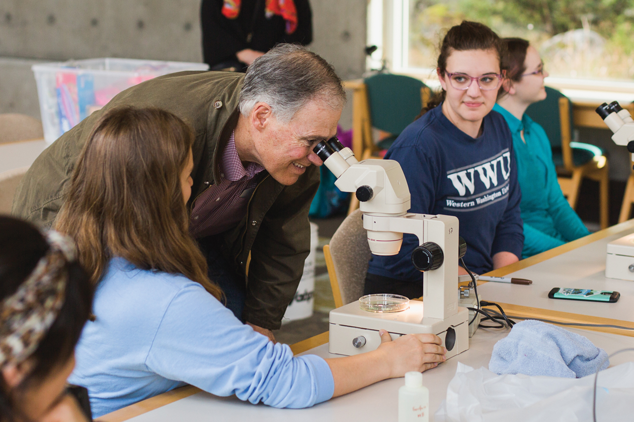 Governer Jay Inslee looking through a microscope with nearby students