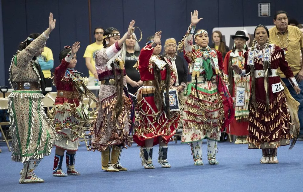 A group of Native American women in Jingle Dresses with hands raised