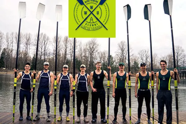  Eight male members of the WWU crew team stand on a dock holding their oars.