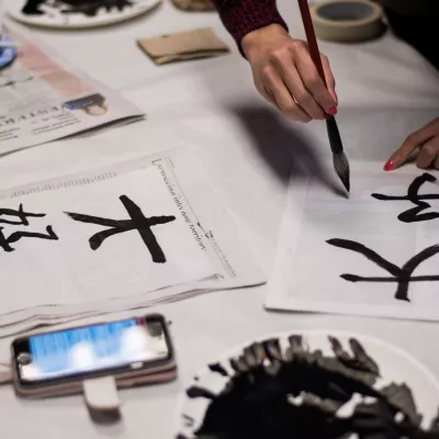 Hands drawing Japanese characters with brushes on white paper.