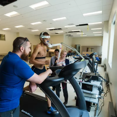 A person with devices attached to their head runs on a treadmill while three others look on, monitoring their vital signs.