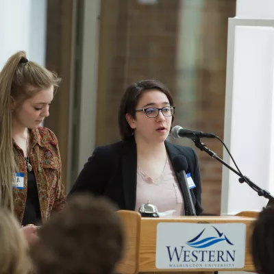 Two students stand and speak at a podium with the Western logo.