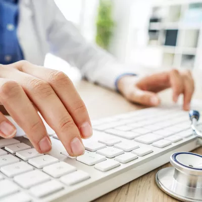 Close-up of a medical professional typing on a keyboard with a stethoscope next to them.
