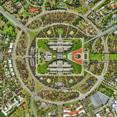 Aerial view of the Canberra Parliament House, Australia. A large green rectangular campus with large boomerang walls surrounding parliament buildings. All surrounded by concentric circles of roads. The parliament is clearly what the rest of the city revolves around.