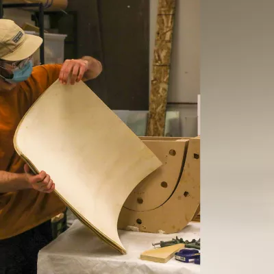 A student designing, prototyping, and building a modern bent plywood chair with upholstery.