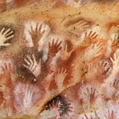 Hand stencil cave paintings cover the walls of a cave in white, black, red, and brown pigment.