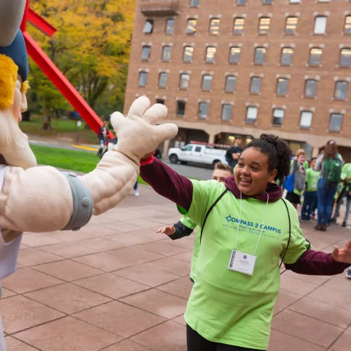 A 5th grade student of color high-fives Victor the Viking, WWU's mascot.