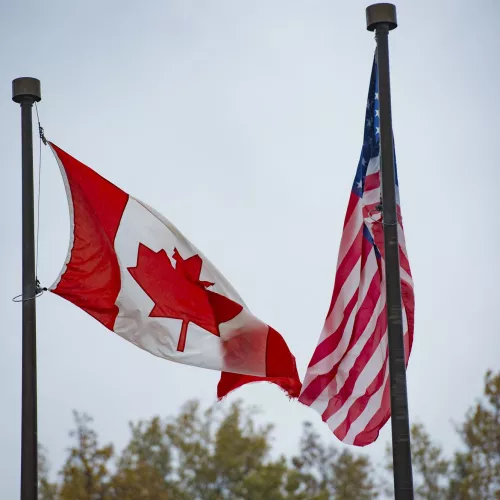 Two flagpoles, one with a Canadian flag and one with an American flag.