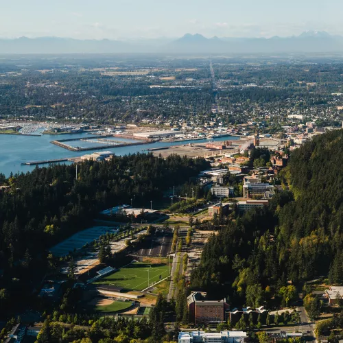 An aerial view of Western's campus flanked on the left by blue Bellingham bay and on the right by forested Sehome arboretum