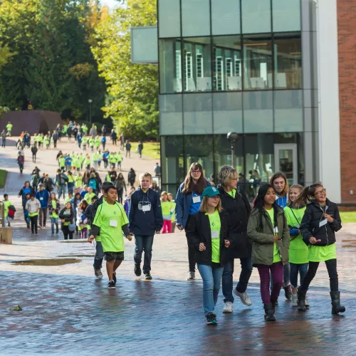 A group of children wearing brightly colored shirts walk on Western's campus