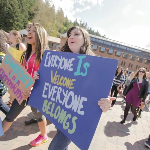 A group of students carry signs and flags through Western's campus, one sign reading "Everyone is Welcome, Everyone Belongs".