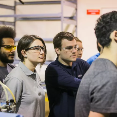 A group of students wearing safety eyewear stand in a lab.