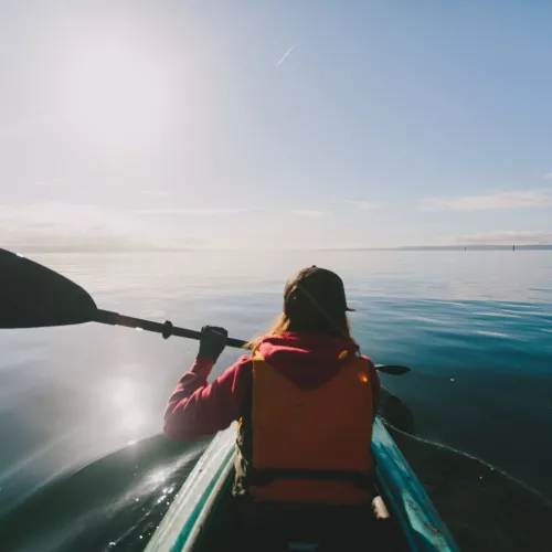 A kayaker paddles through calm waters, as viewed from the back of a tandem kayak.