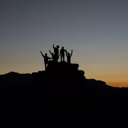 Silhouettes of people posing on a rocky landscape, with the sun setting in the background.