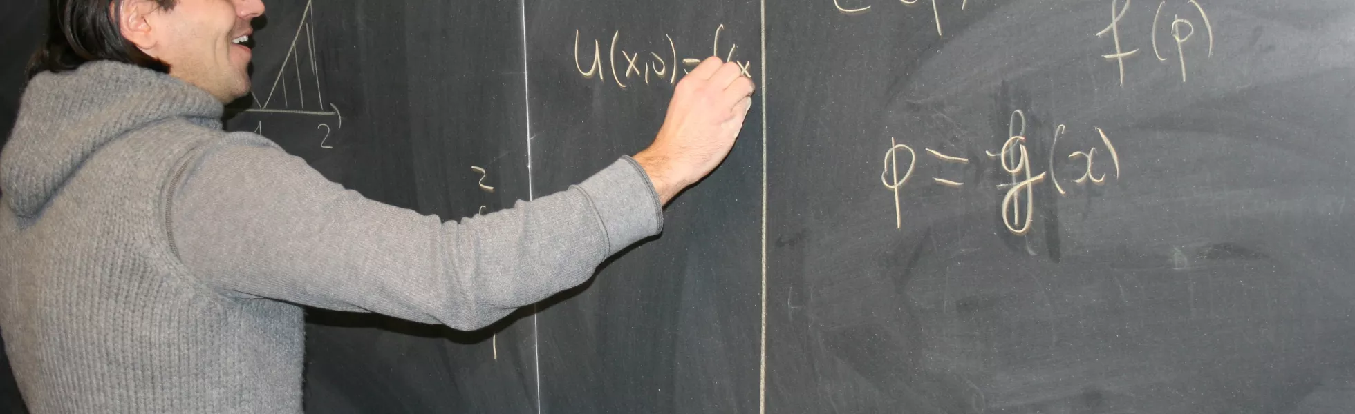 A student writing statistic equations on a blackboard with chalk.