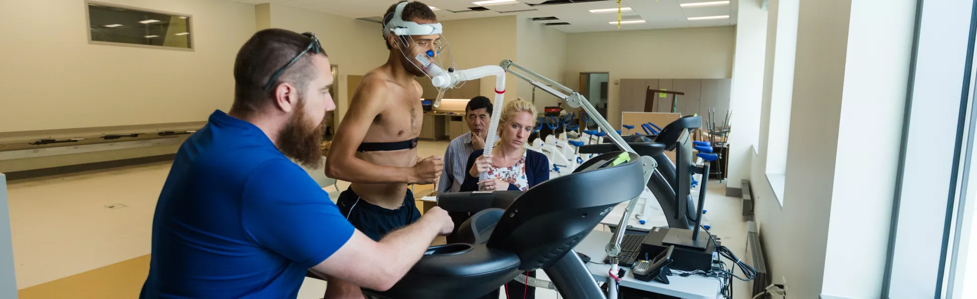 A person with devices attached to their head runs on a treadmill while three others look on, monitoring their vital signs.