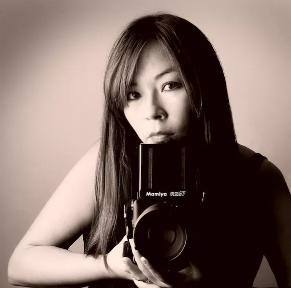 Matika holding a camera in front of her in a sepia tone on the photo