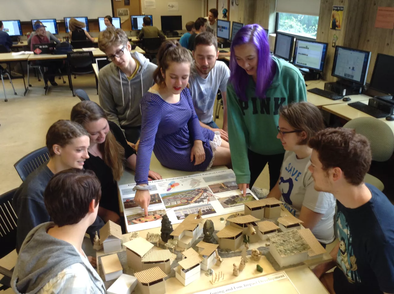 A group of students sitting and standing around a miniature model of a housing settlement.