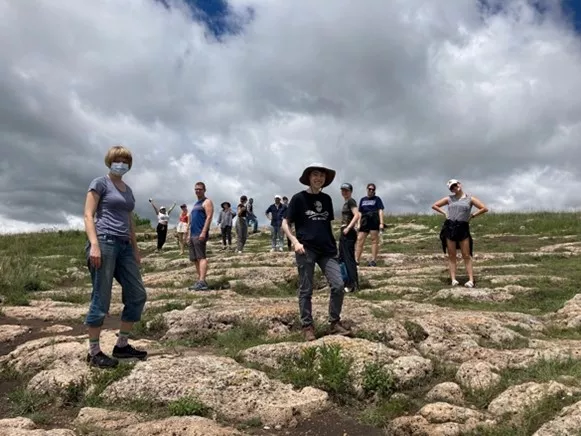 Students standing spread out on a rocky and grassy hill.