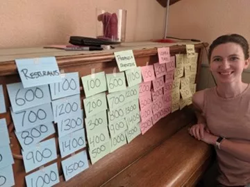 A student sitting in front of a homemade game of Jeopardy, created out of notecards taped to an upright piano.