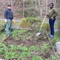 Two students stand over a garden pallet, one of them is holding a shovel.
