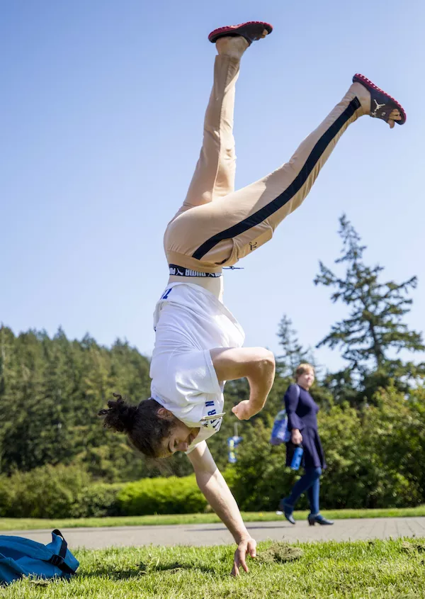A student executes a handstand on a sunny day while wearing flip flops