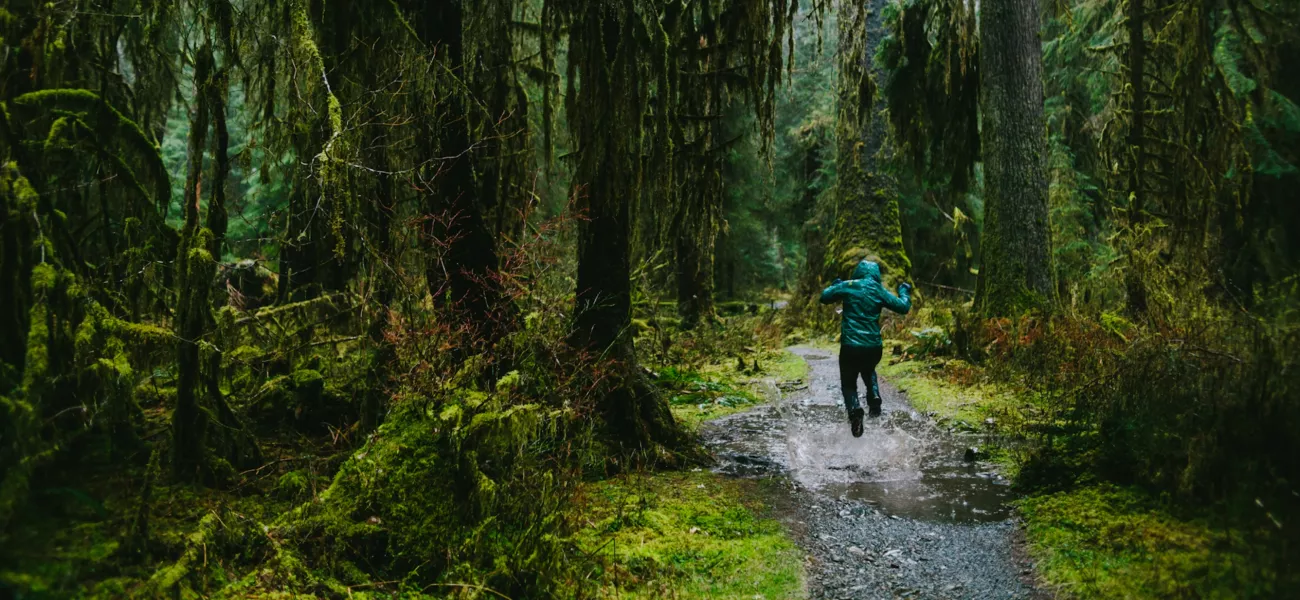 A raincoat clad person jumps over a puddle in the rain forest