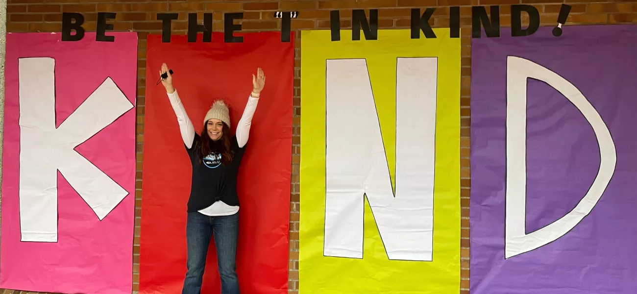 A life-sized, colorful poster of the word KIND with a person standing, arms outstretched, as the letter "I".