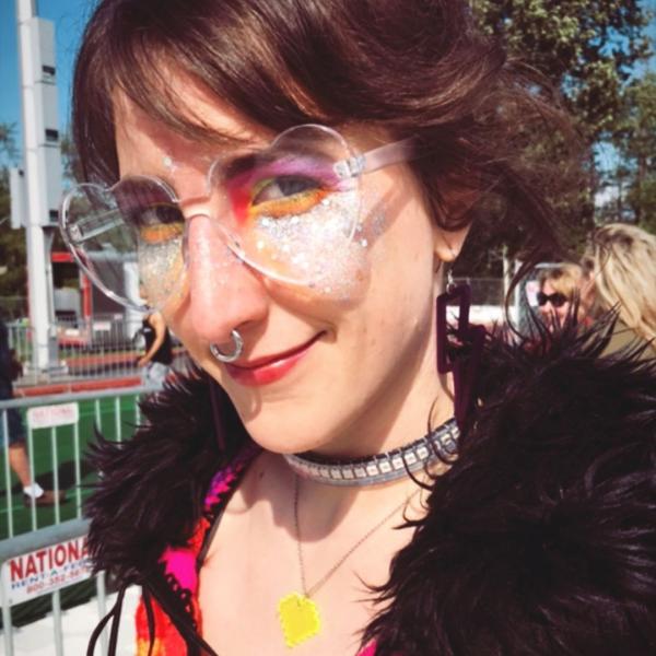Stephanie smiles, wearing heart-shaped glasses and rainbow eyeshadow