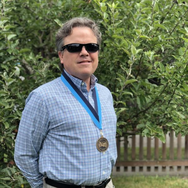 David wears a 2020 celebration of excellence medal while standing in front of his apple tree.
